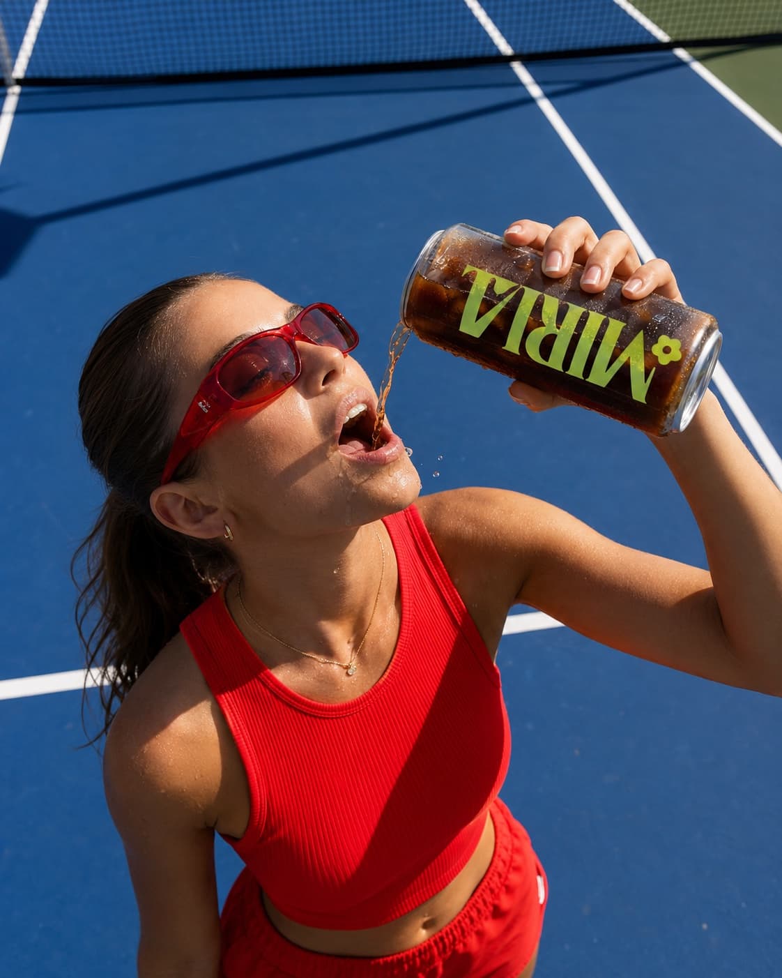 A tennis player courtside pouring an iced drink from a clear custom-printed can