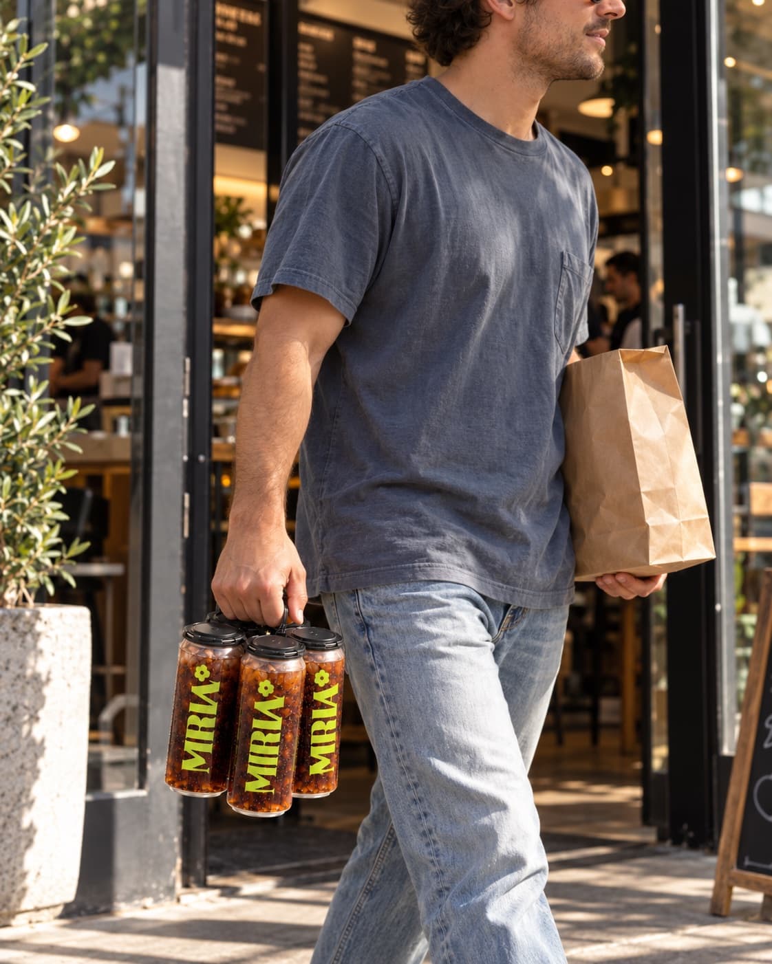 A customer walking out of a café with a takeout bag and a four-pack of sealed clear cans